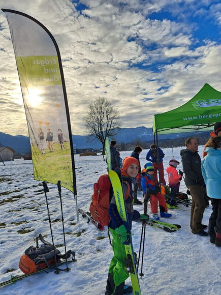 Kinder mit Ski an einem Bergsportfachverband-Stand vor einer Bergkulisse