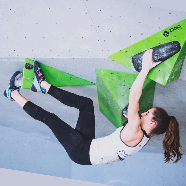 Athletin klettert an einem Boulder mit grünen Volumen und schwarzen Griffen